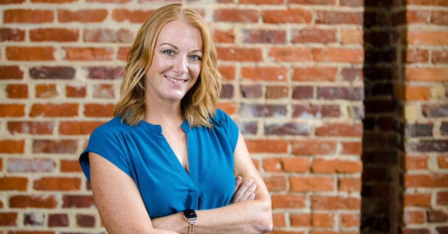Heather Winkle, Capital One Senior VP & Head of Experience Design, stands with her arms crossed in front of a brick wall